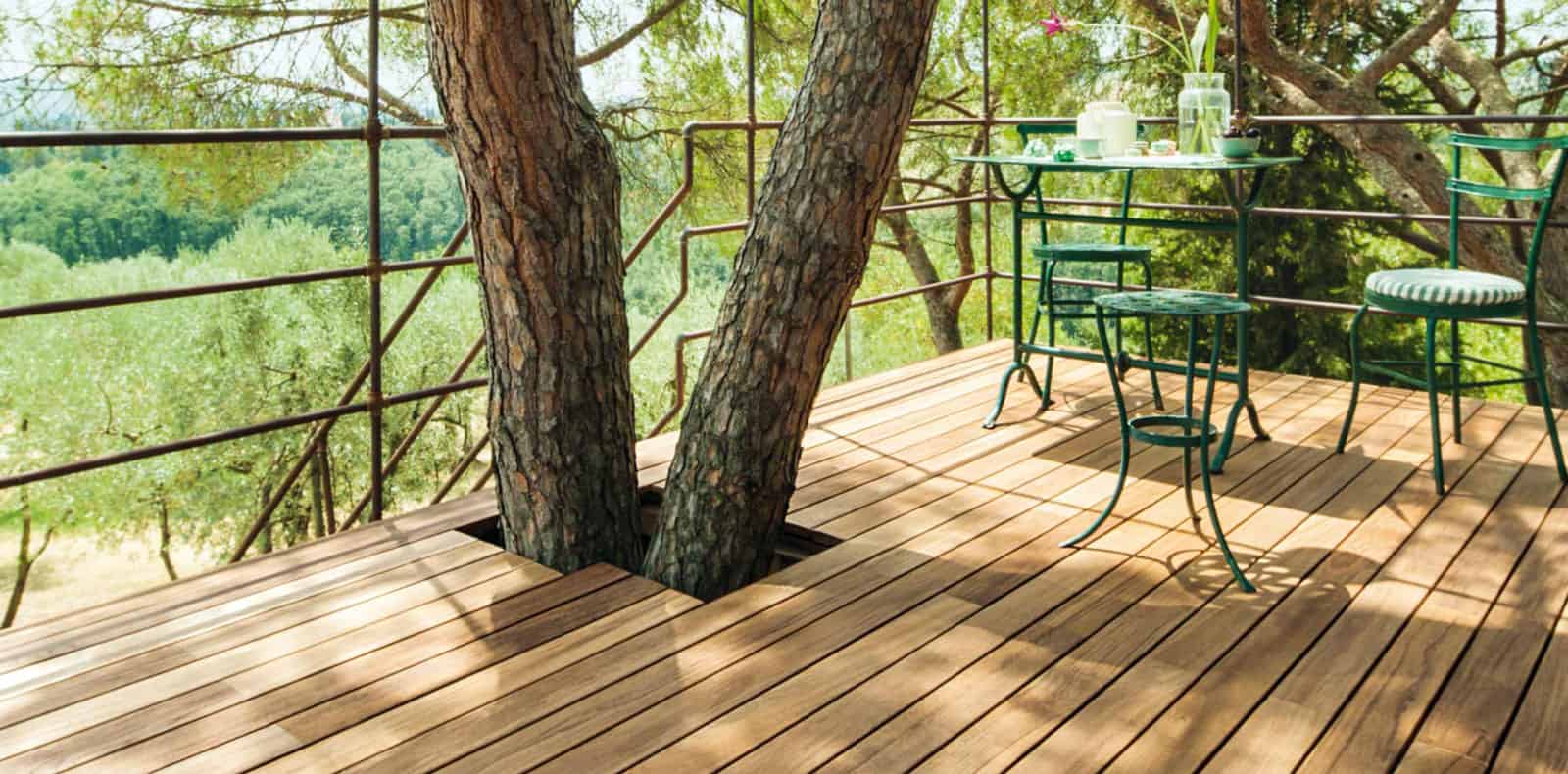 Parquet Listone Giordano su un deck all'esterno in mezzo agli alberi verdi, con un albero che passa attraverso un buco specifico nel pavimento e un tavolino e sedie verdi